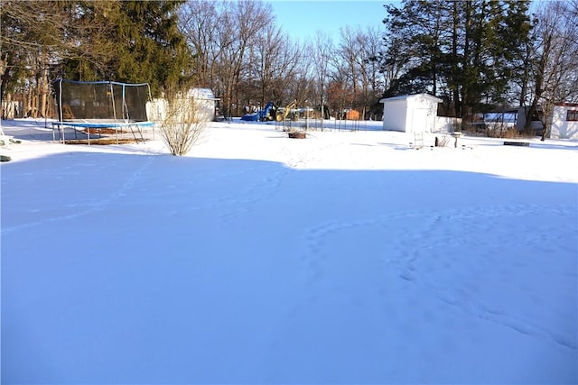 yard layered in snow featuring a trampoline and a storage unit