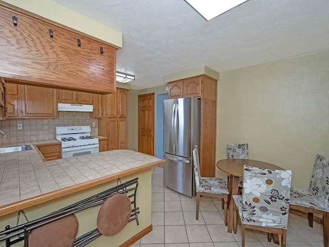 kitchen featuring tasteful backsplash, tile countertops, gas range gas stove, light tile patterned floors, and stainless steel fridge