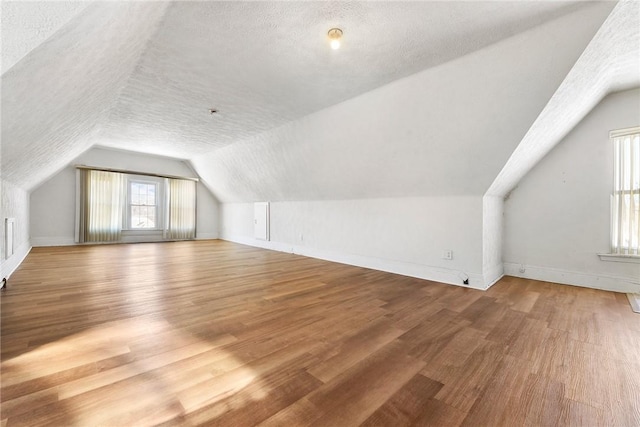 additional living space featuring lofted ceiling, wood-type flooring, and a textured ceiling