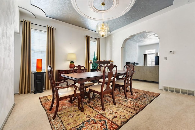 dining area with light colored carpet, a tray ceiling, and a notable chandelier