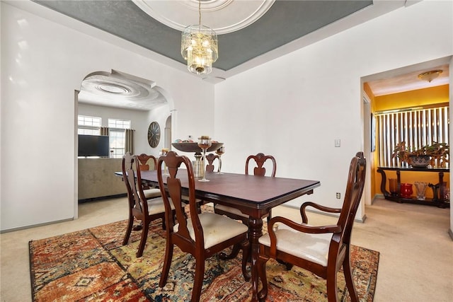 dining area featuring an inviting chandelier, light colored carpet, and a tray ceiling