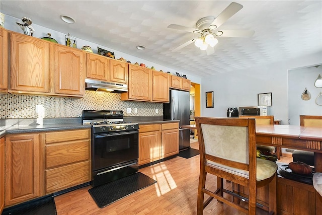 kitchen with black gas range oven, decorative backsplash, stainless steel refrigerator, and light hardwood / wood-style floors