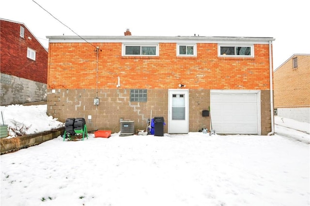 snow covered rear of property with a garage and cooling unit