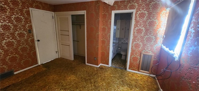 unfurnished bedroom featuring a closet, ensuite bathroom, and carpet