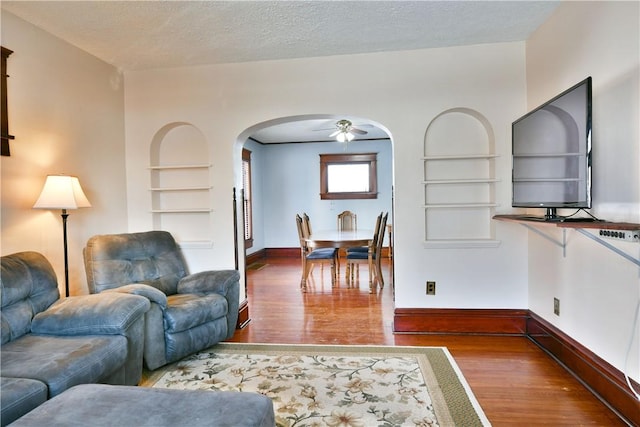 living room featuring hardwood / wood-style flooring, a textured ceiling, built in features, and ceiling fan