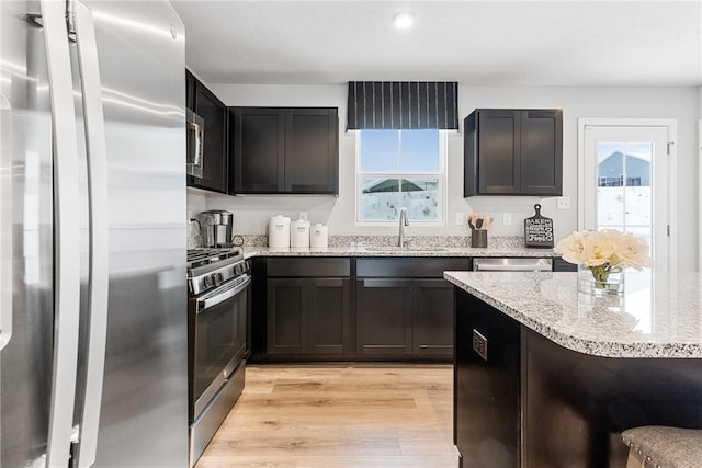 kitchen featuring stainless steel appliances, light hardwood / wood-style flooring, light stone counters, and sink