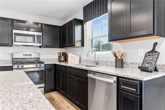 kitchen featuring stainless steel appliances, light stone counters, a sink, and light wood-type flooring