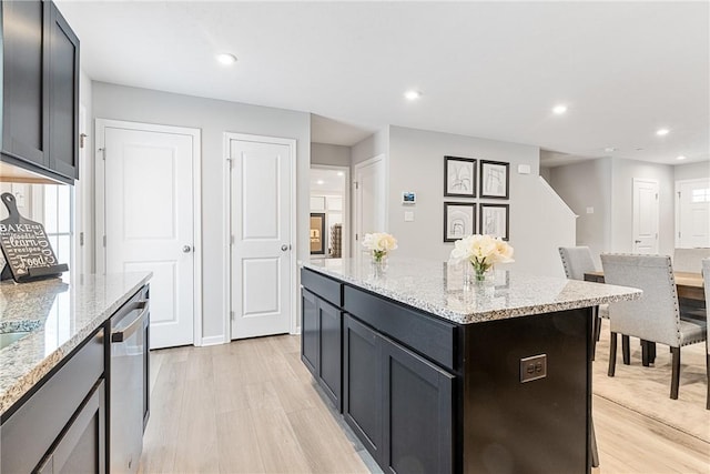 kitchen with stainless steel dishwasher, light stone countertops, light hardwood / wood-style floors, and a center island