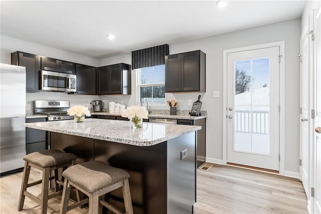 kitchen with appliances with stainless steel finishes, a breakfast bar, light wood finished floors, and a center island