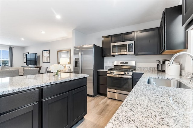 kitchen with open floor plan, light stone counters, a sink, light wood finished floors, and appliances with stainless steel finishes