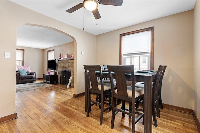 dining area featuring ceiling fan, light wood-type flooring, and a fireplace