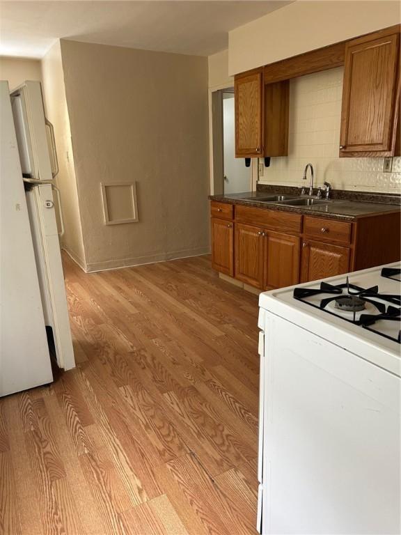 kitchen with tasteful backsplash, light wood-type flooring, sink, and white appliances