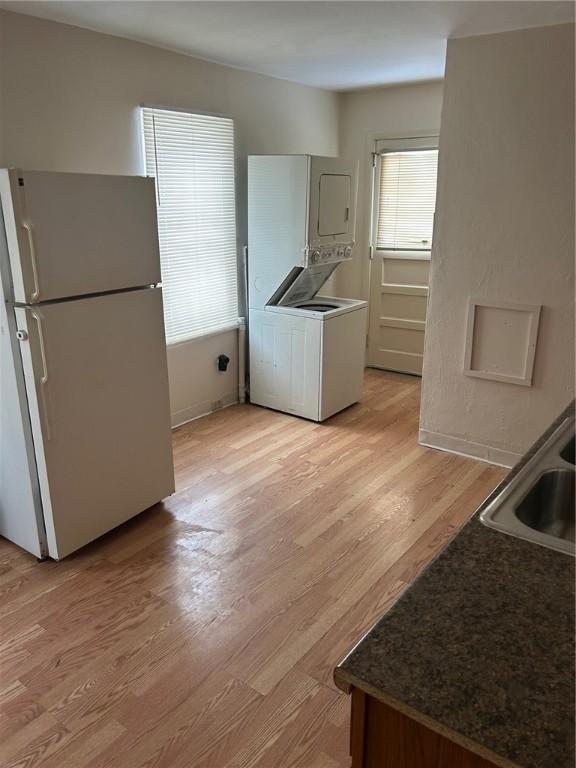 kitchen with sink, white refrigerator, stacked washer and clothes dryer, and light wood-type flooring