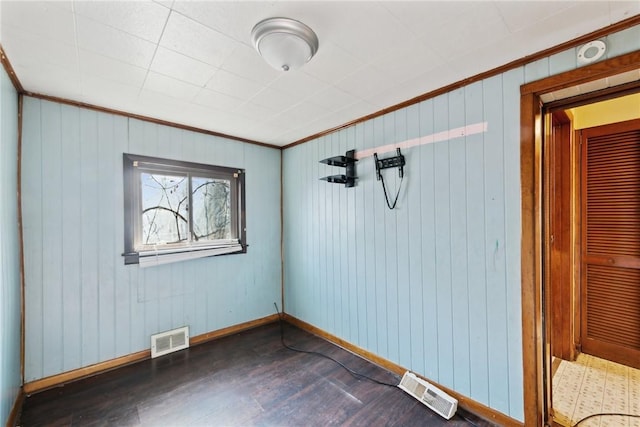 empty room with dark hardwood / wood-style flooring, ornamental molding, and wood walls