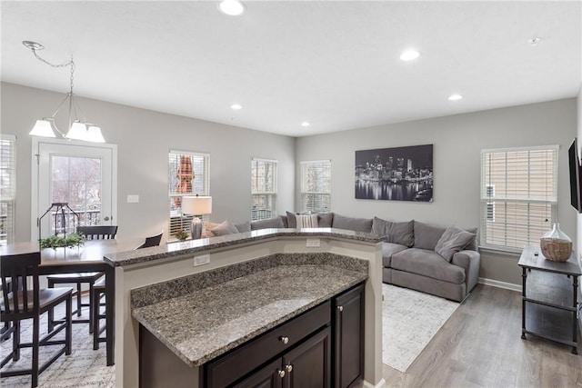 kitchen featuring a notable chandelier, pendant lighting, light hardwood / wood-style floors, dark brown cabinetry, and light stone countertops