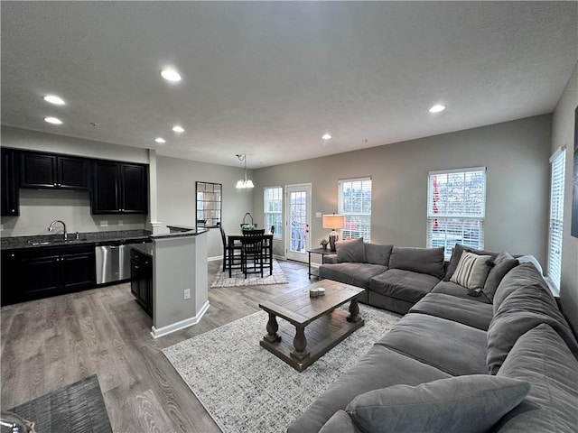 living room with a wealth of natural light, light wood-type flooring, a notable chandelier, and sink