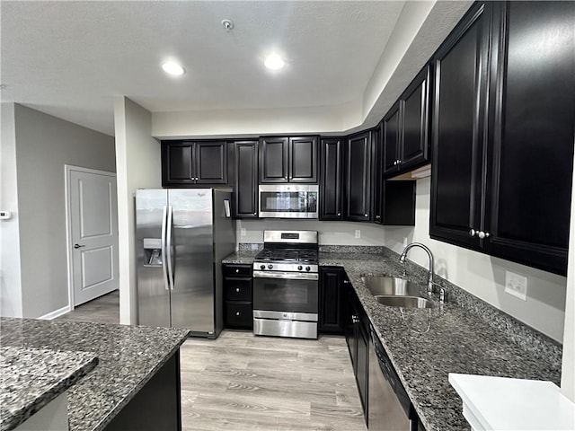 kitchen with sink, stainless steel appliances, dark stone counters, and light wood-type flooring