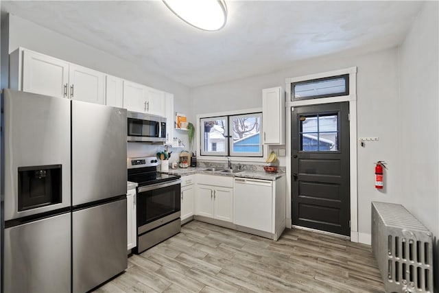 kitchen with light hardwood / wood-style floors, sink, white cabinetry, radiator, and appliances with stainless steel finishes