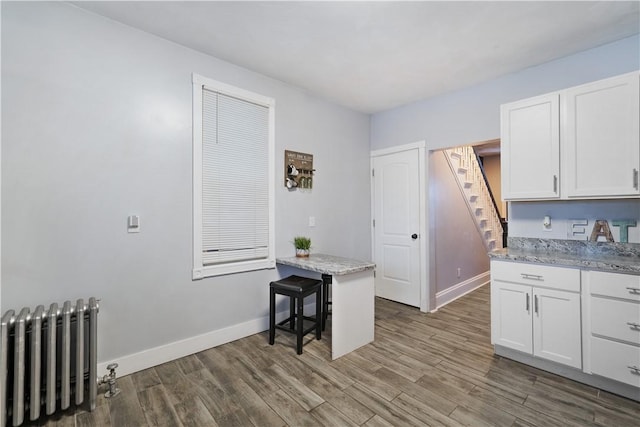 kitchen with radiator, dark wood-type flooring, white cabinets, and light stone counters