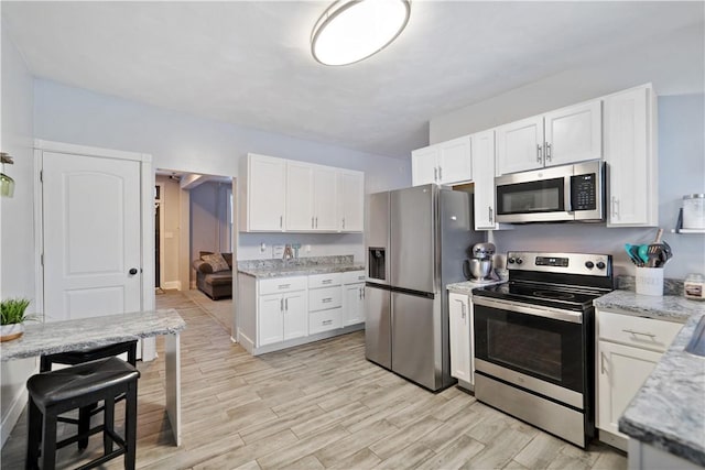 kitchen with light stone countertops, white cabinetry, and appliances with stainless steel finishes