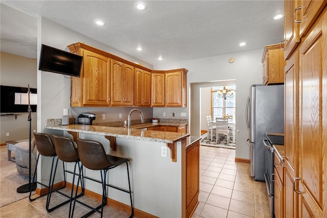 kitchen featuring a kitchen breakfast bar, kitchen peninsula, a chandelier, light stone counters, and light tile patterned floors