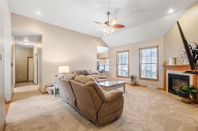 living room featuring ceiling fan, light colored carpet, a tiled fireplace, and vaulted ceiling