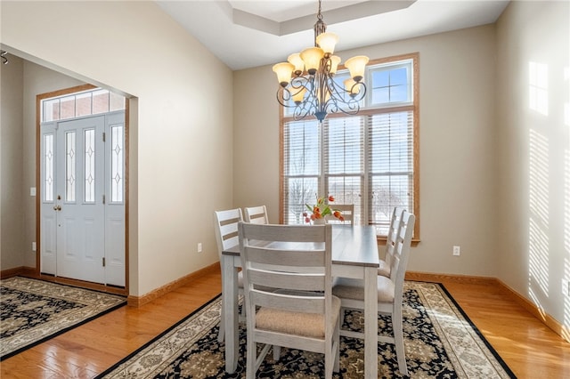 dining space featuring a raised ceiling, wood-type flooring, and an inviting chandelier