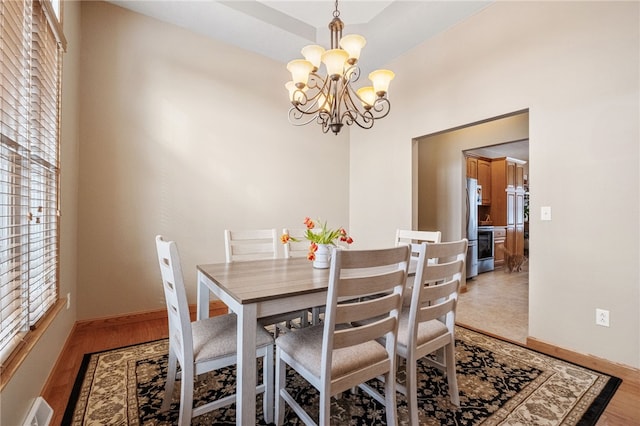 dining area with a tray ceiling, an inviting chandelier, and light hardwood / wood-style floors