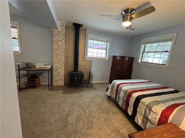 carpeted bedroom with ceiling fan, a wood stove, and wood walls