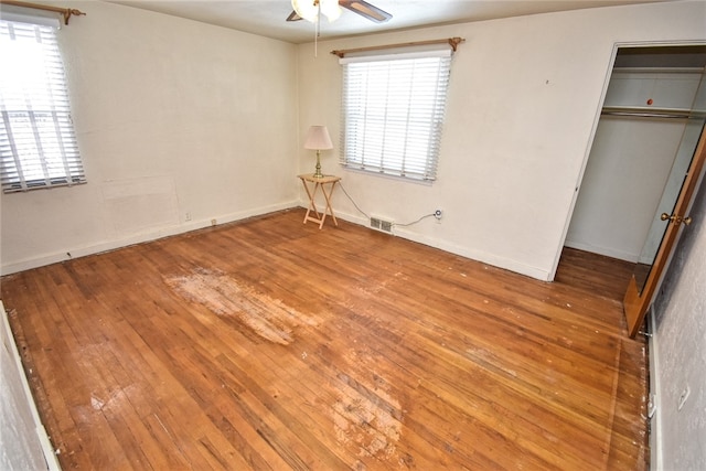 unfurnished bedroom with ceiling fan, multiple windows, wood-type flooring, and a closet