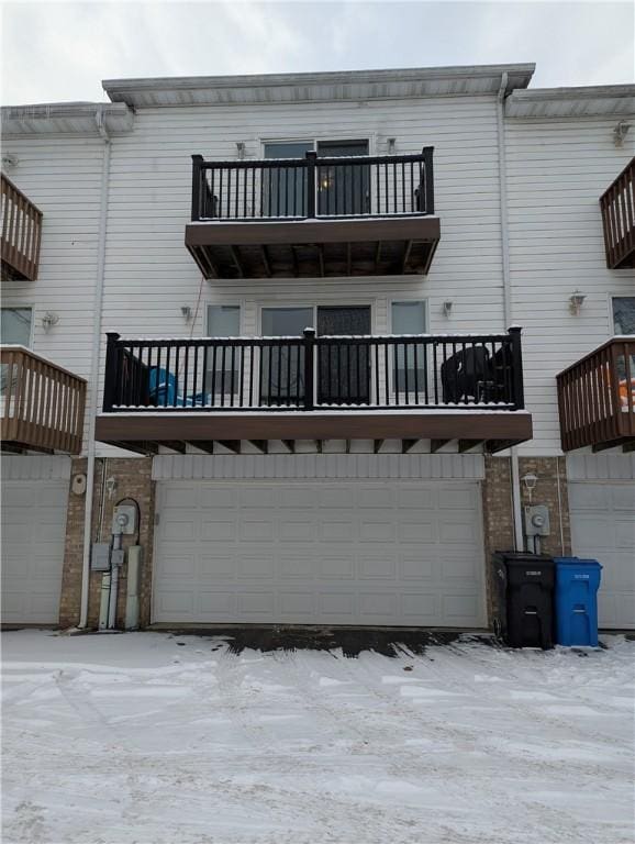 snow covered back of property with a balcony and a garage