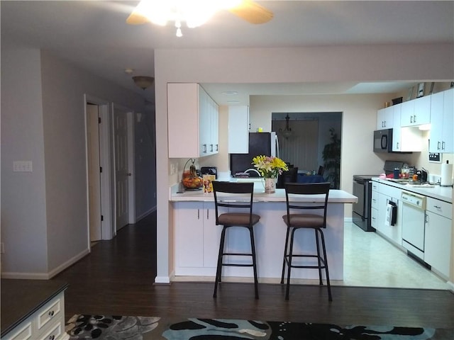 kitchen featuring dishwasher, a kitchen bar, white cabinetry, stainless steel refrigerator, and electric range