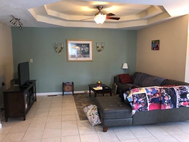 living room with ceiling fan, light tile patterned floors, and a raised ceiling