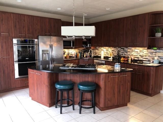 kitchen with appliances with stainless steel finishes, a center island, decorative backsplash, sink, and a breakfast bar