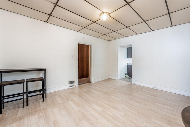 empty room with a drop ceiling and light hardwood / wood-style flooring