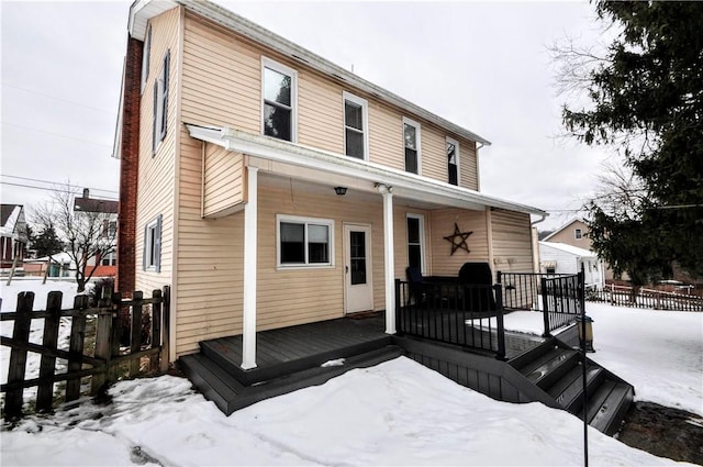 snow covered rear of property featuring covered porch