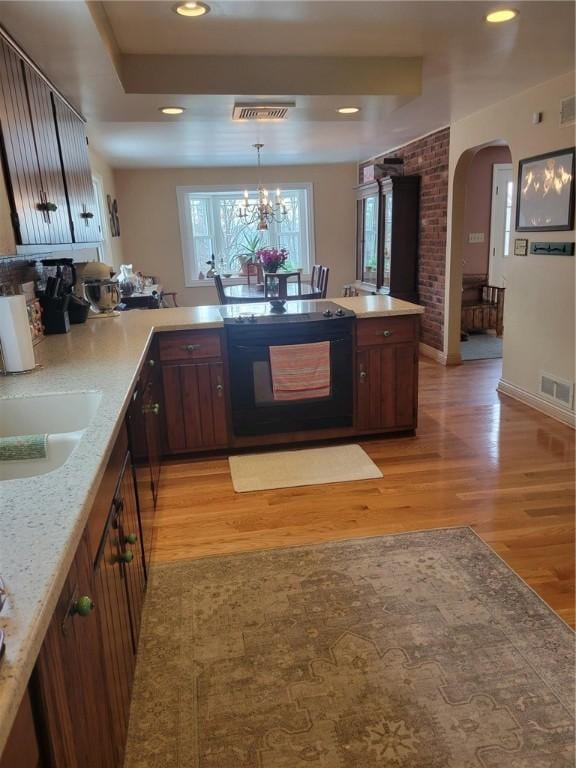 kitchen with decorative light fixtures, a notable chandelier, black appliances, sink, and light hardwood / wood-style flooring