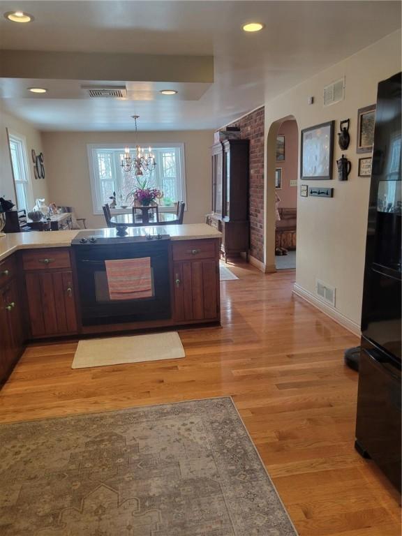 kitchen with dark brown cabinetry, decorative light fixtures, a chandelier, light hardwood / wood-style floors, and black appliances