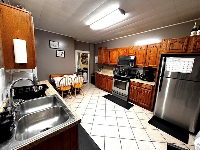 kitchen with sink, backsplash, light tile patterned flooring, and appliances with stainless steel finishes