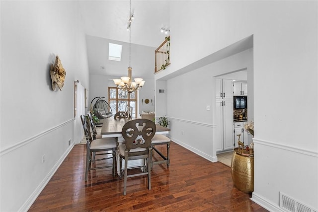 dining room with high vaulted ceiling, dark hardwood / wood-style floors, a skylight, and a notable chandelier