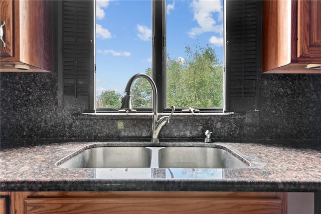 interior details featuring sink, tasteful backsplash, and dark stone countertops