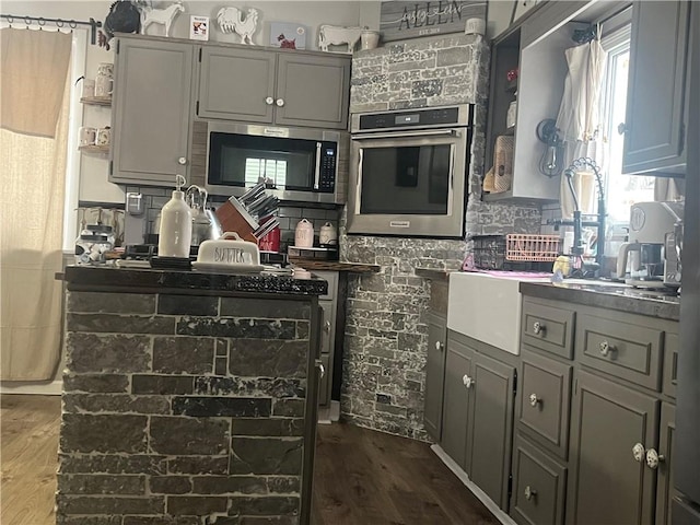 kitchen with appliances with stainless steel finishes, dark hardwood / wood-style flooring, and gray cabinetry