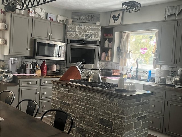 kitchen featuring appliances with stainless steel finishes, gray cabinets, a center island, and tasteful backsplash