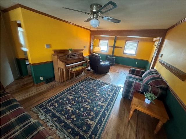 living room featuring ceiling fan, ornamental molding, a wood stove, and hardwood / wood-style flooring