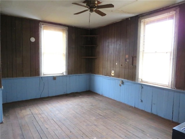 empty room featuring ceiling fan, light hardwood / wood-style floors, and wood walls