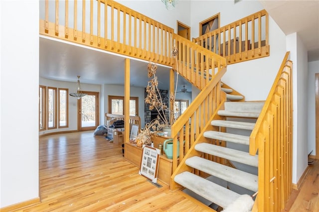 staircase with ceiling fan with notable chandelier, wood-type flooring, and a stone fireplace