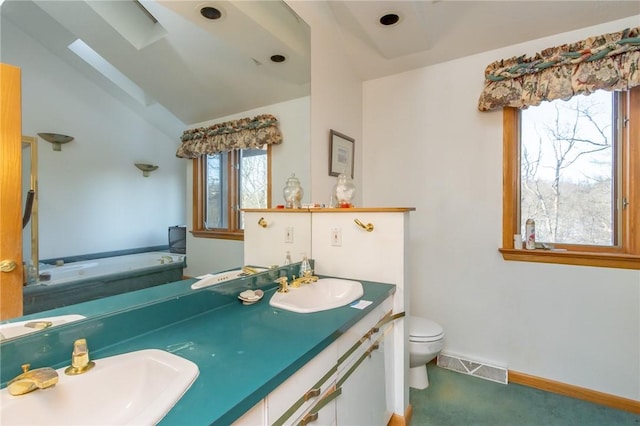 bathroom featuring a tub, vanity, vaulted ceiling with skylight, and toilet