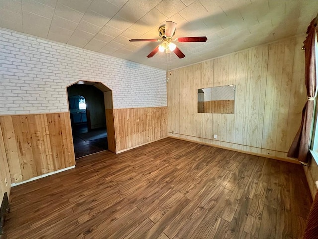 unfurnished room featuring ceiling fan, dark wood-type flooring, brick wall, and wooden walls