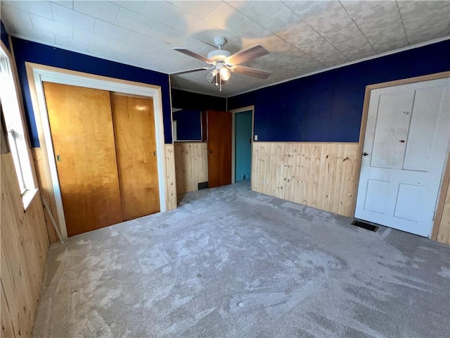 unfurnished bedroom with ceiling fan, carpet flooring, a closet, and wooden walls