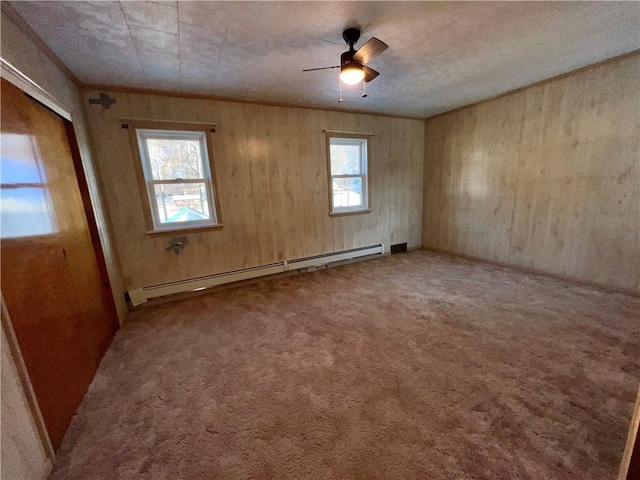 unfurnished room featuring ceiling fan, a wealth of natural light, wooden walls, and a baseboard radiator